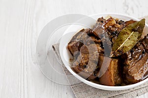 Homemade Filipino Adobo Pork in a bowl on a white wooden surface, side view. Space for text