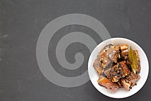 Homemade Filipino Adobo Pork in a white bowl on a black background, top view. Flat lay, overhead, from above. Copy space
