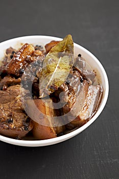 Homemade Filipino Adobo Pork in a white bowl on a black surface, low angle view. Close-up