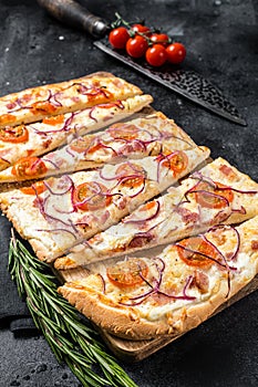 Homemade Flammkuchen or tarte flambee with cream cheese, bacon, tomato and onions. Black background. Top view