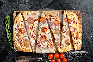 Homemade Flammkuchen or tarte flambee with cream cheese, bacon, tomato and onions. Black background. Top view