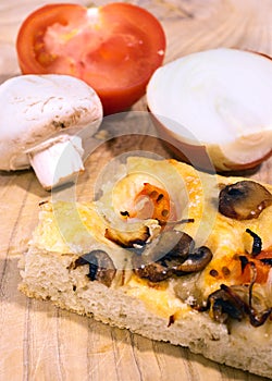 Homemade focaccia with onion, tomato and mushrooms on a wooden table. Traditional italian bread