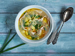 Homemade food, chicken soup with potatoes, pasta and green onions in a deep plate on a blue wooden table