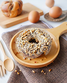 Homemade food fresh bakery, Closeup delicious chocolate donut almond peanut topping served on wooden dish, spoon, fork on napery