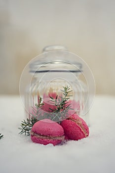 Homemade french pink macarons with raspberry cream on frozen snow background. Sweet delicious cookie in glass jar