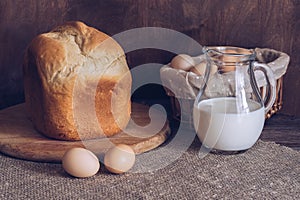 Homemade fresh bread, milk in a jug and eggs on a wooden table.