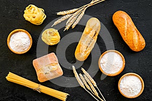 Homemade fresh bread and pasta near flour in bowl and wheat ears on black background top view