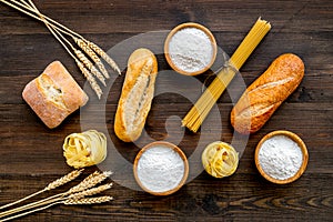 Homemade fresh bread and pasta near flour in bowl and wheat ears on dark wooden background top view