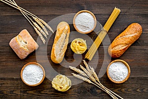 Homemade fresh bread and pasta near flour in bowl and wheat ears on dark wooden background top view