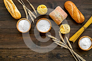 Homemade fresh bread and pasta near flour in bowl and wheat ears on dark wooden background top view space for text
