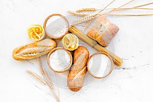 Homemade fresh bread and pasta near flour in bowl and wheat ears on white stone background top view