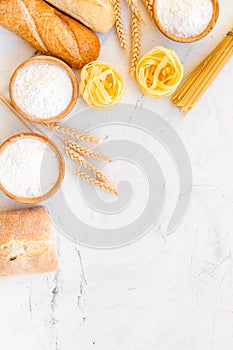 Homemade fresh bread and pasta near flour in bowl and wheat ears on white stone background top view space for text