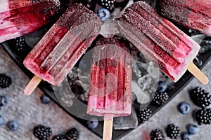 Homemade fresh frozen blueberry and blackberry popsicles on black plate with ice sitting on stone