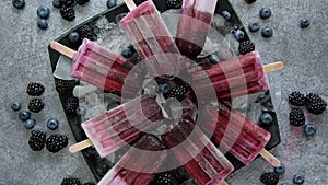 Homemade fresh frozen blueberry and blackberry popsicles on black plate with ice sitting on stone