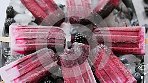 Homemade fresh frozen blueberry and blackberry popsicles on black plate with ice sitting on stone