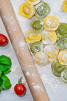Homemade fresh Italian ravioli pasta on white wood table with flour, basil, tomatoes,background,top view
