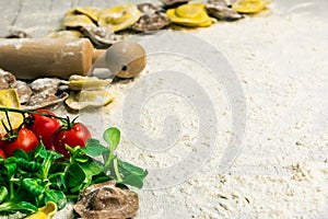 Homemade fresh Italian ravioli pasta on white wood table with flour, basil, tomatoes,background,top view