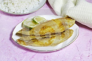 homemade fried fish lemon sole with rice in white plate on grunge pink background.