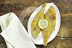 homemade fried fish lemon sole in white plate on wood table.