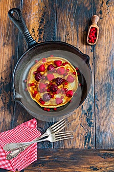 Homemade fried pancakes on a black cast iron skillet. Above are berries, raspberries, cranberries and blackberries.