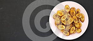 Homemade fried plantains on a pink plate on a black surface, overhead view. Flat lay, from above, top view. Space for text