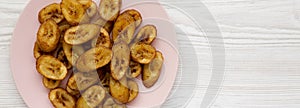 Homemade fried plantains on a pink plate on a white wooden surface, top view. Flat lay, overhead, from above. Space for text