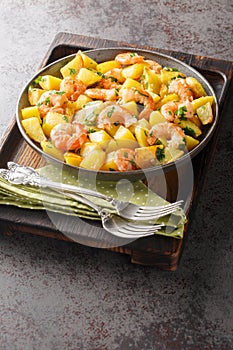 Homemade fried potatoes with garlic, herbs and shrimp close-up in a plate. Vertical