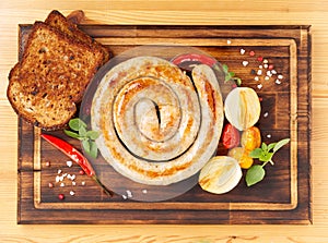 homemade fried sausage, spiral shape, with vegetables and bread on dark wooden chopping board, top view