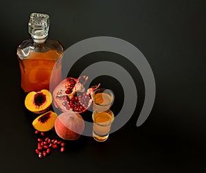 Homemade fruit liqueur in a glass bottle and two glasses on a black background, next to pieces of ripe pomegranate and a broken