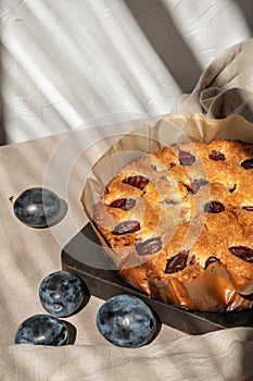 Homemade fruit plum pie, original plum torte on beige table with sunlight shadows on wall background. Sweet delicious bakery