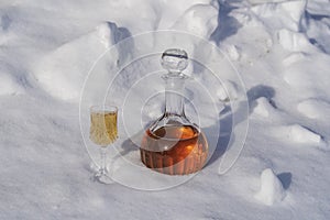 Homemade fruit tincture in a glass bottle and a wine crystal glass on a snow and white background