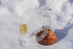 Homemade fruit tincture in a glass bottle and a wine crystal glass on a snow and white background
