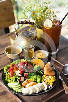 Homemade fruit vegetable salad, honey mustard, tomato,strawberry,orange,apple,banana,maize and sausage in bowl  with lemon tea on