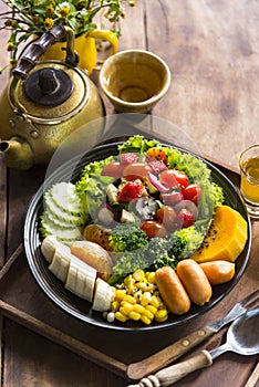 Homemade fruit vegetable salad, honey mustard, tomato,strawberry,orange,apple,banana,maize and sausage in bowl  with lemon tea on