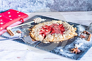 Homemade galette pie cake with strawberries and almond, placed on black desk and wooden table. Red towel with cooking tools on the