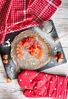 Homemade galette pie cake with strawberries and almond, placed on black desk and wooden table. Red towel with cooking tools on the