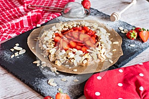 Homemade galette pie cake with strawberries and almond, placed on black desk and wooden table. Red towel with cooking tools on the