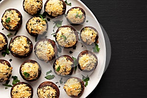 Homemade Garlic Parmesan-Stuffed Mushrooms on a plate on a black background, top view. Copy space