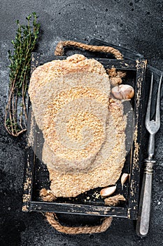 Homemade German Wiener Raw schnitzel in a wooden tray. Black background. Top view
