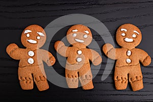 Homemade gingerbread cookies covered with icing, three gingerbread men waving hand and smiling, on black wooden background