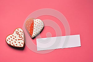 Homemade gingerbread hearts with an empty paper for your text on pink background. Valentine cookies hearts. Edible Valentine`s Da
