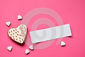 Homemade gingerbread hearts with an empty paper for your text on pink background. Valentine cookies hearts. Edible Valentine`s Da