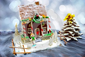 Homemade gingerbread house, gingerbread Christmas tree and a sugar mastic snowman on background of defocused silver lights