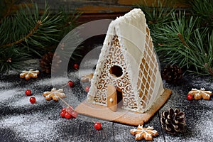Homemade gingerbread house with pine branches, cones and biscuits on dark background. European Christmas traditions. Xmas holiday photo