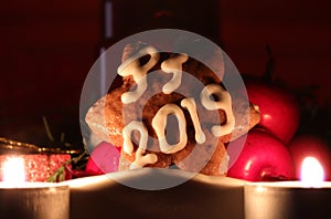 Homemade gingerbread star covered with white icing and letters PF 2019 leaning againts fruits with two candles