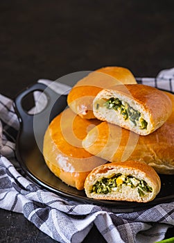 Homemade golden pies with green onion and egg on a black plate on a dark concrete background. Unsweetened pastries