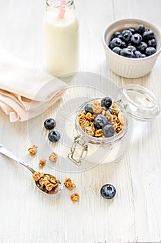 Homemade granola with blueberries in jar on white kitchen background