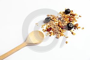 Homemade granola or granola with dried berries and nuts sprinkled on a white plate next to a wooden spoon. Home-made food, healthy