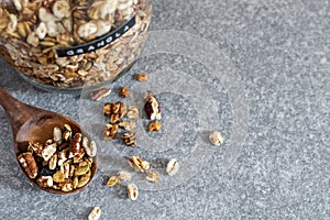 Homemade granola with pecan nuts in glass jar, selective focus, gray background