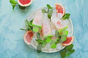 Homemade grapefruit popsicles with grapefruit slices on a mint wooden background.